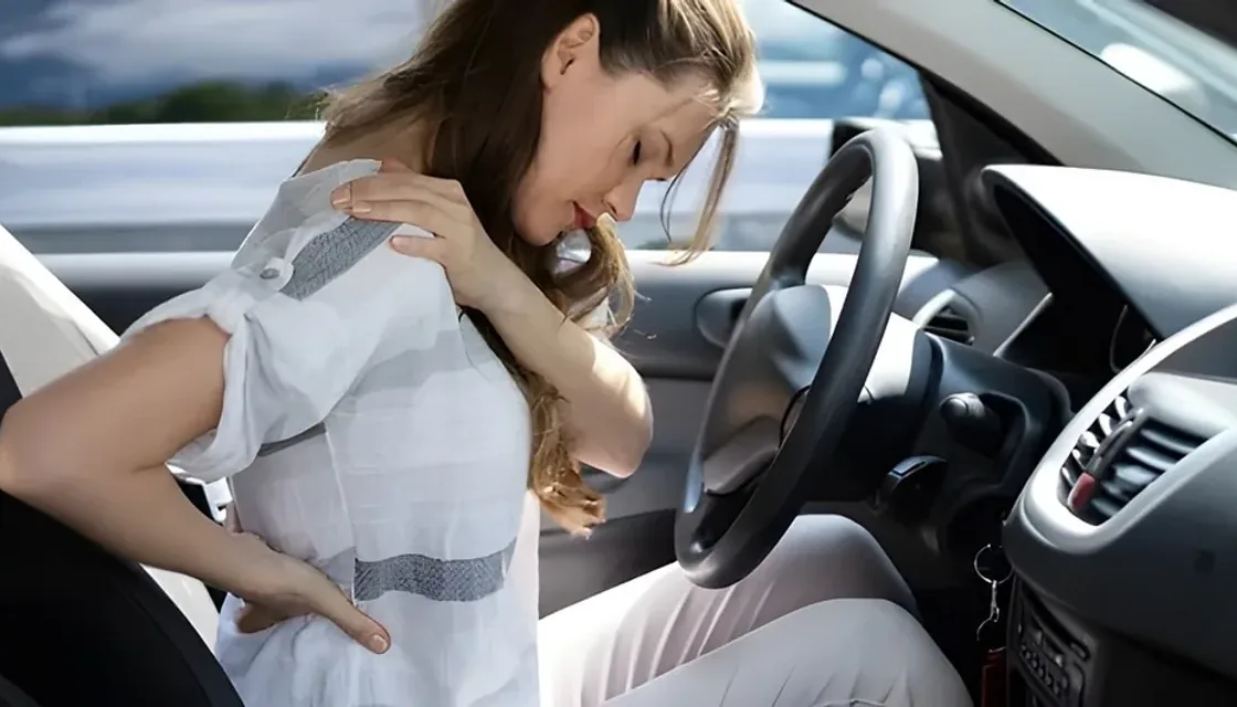 A driver holding her neck and back after a car accident while seated in her vehicle