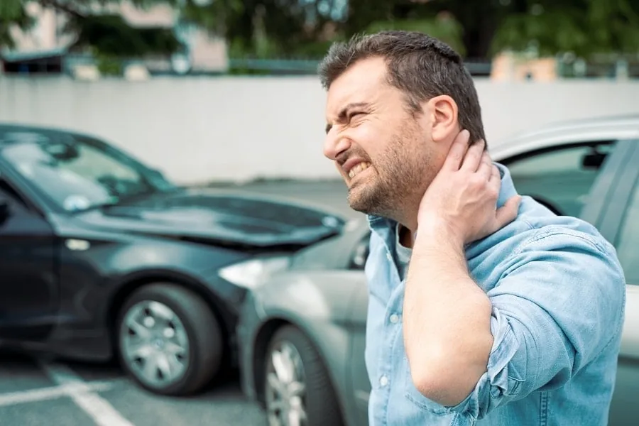 A man with neck pain beside damaged cars after an auto accident in Tampa